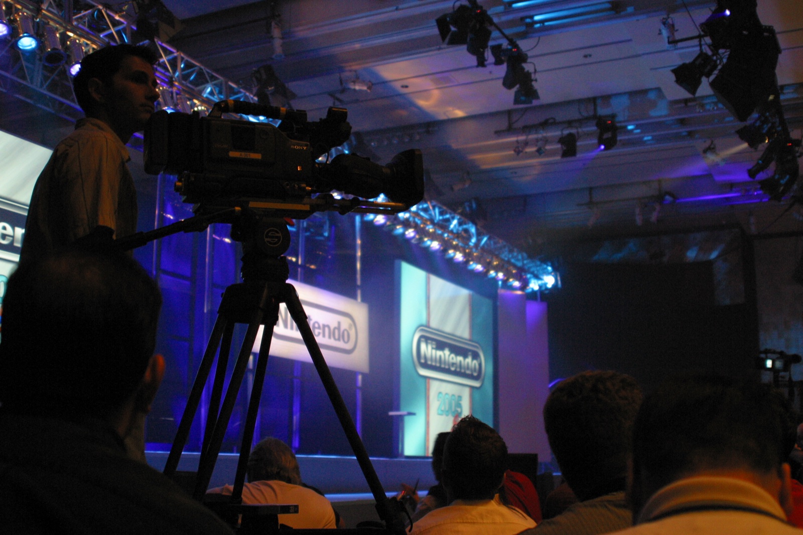 A camera operator sets up at the Nintendo press conference — the stage bathed in blue light.